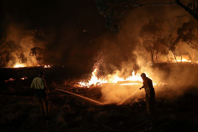 Firefighters work to extinguish flames after a bushfire burnt through the area in Bredbo