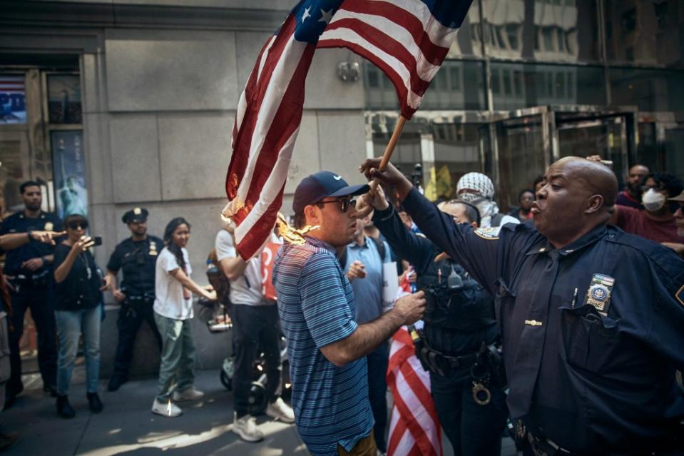 An NYPD cop grabs a US flag set on fire by pro-Palestinian protesters during a demonstration. AP