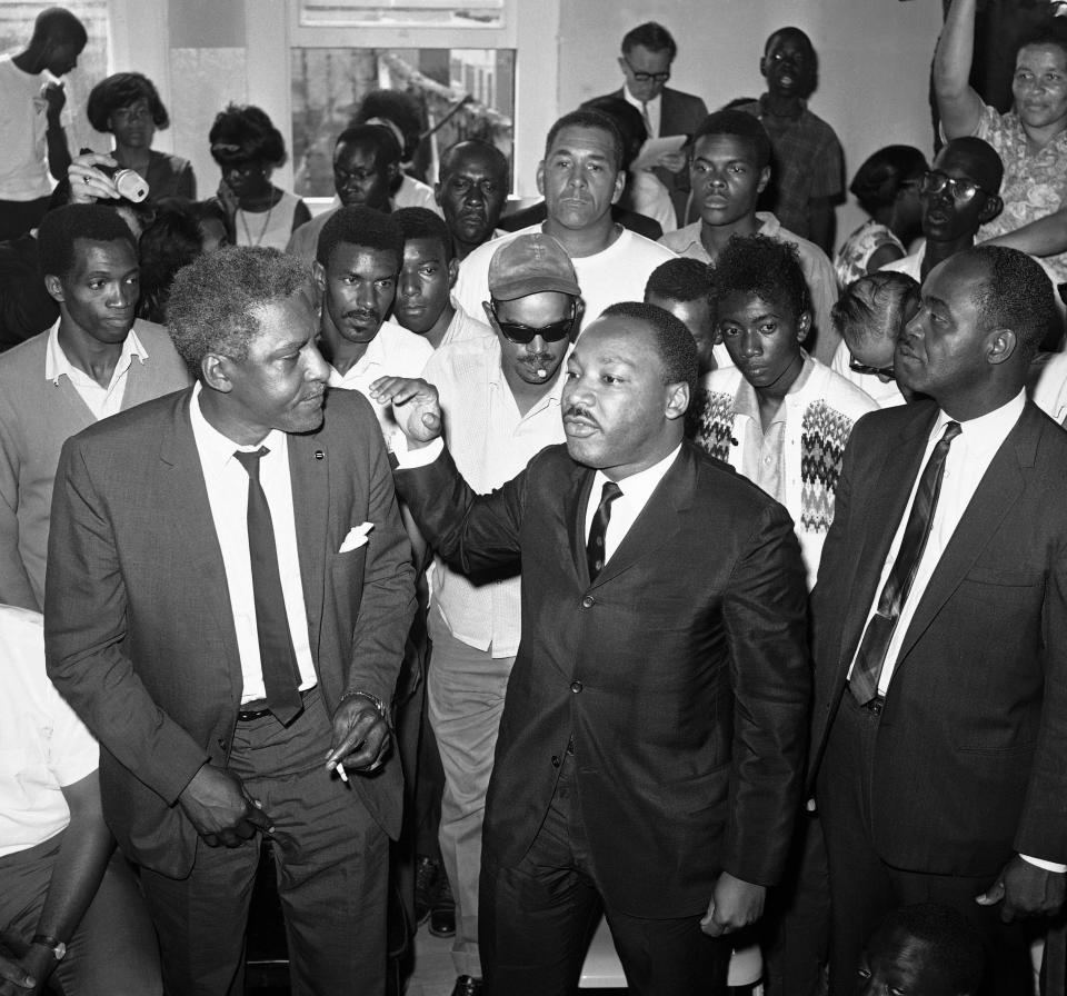 FILE - Dr. Martin Luther King Jr., center, addresses a gathering in the riot-torn area of Los Angeles, Aug. 18, 1965. Bayard Rustin, King's aide, is at left. Black LGBTQ+ political representation has grown by 186% since 2019, according to a 2023 report by the LGBTQ+ Victory Institute. These leaders stand on the shoulders of civil rights leaders such as Rustin. (AP Photo/Don Brinn, File)