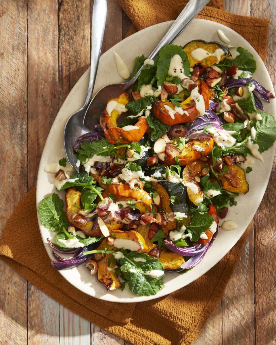 acorn squash salad with tahini vinaigrette on a cream colored oval plate with serving utensils