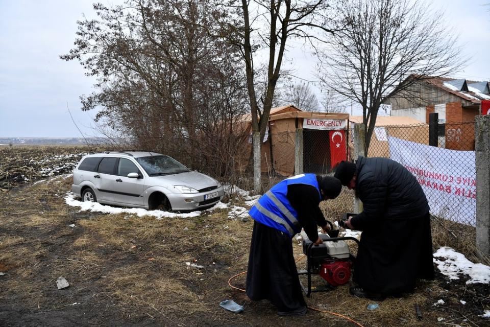 Father Calinic and Father Modest work to fix a generator beside their hospitality tents in Siret (Reuters)