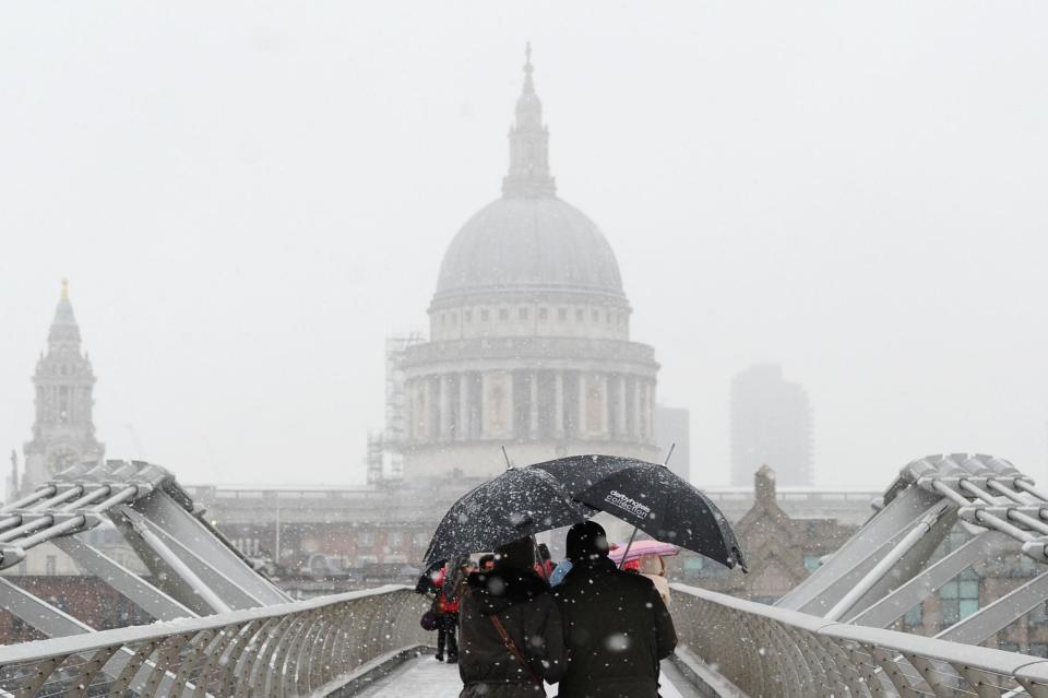 Pedestrians walk over the Millennium Bridge with St Paul's Cathedral pictured in the background as snow falls over central London (December 2017) (AFP/Getty Images)