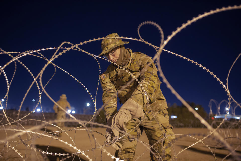 A Texas National Guard soldier ties rows of barbed-wire to be installed near a gate at the border fence in El Paso, Texas, in the early hours of Thursday, May 11, 2023. Migrants rushed across the border hours before pandemic-related asylum restrictions were to expire Thursday, fearing that new policies would make it far more difficult to gain entry into the United States. (AP Photo/Andres Leighton)