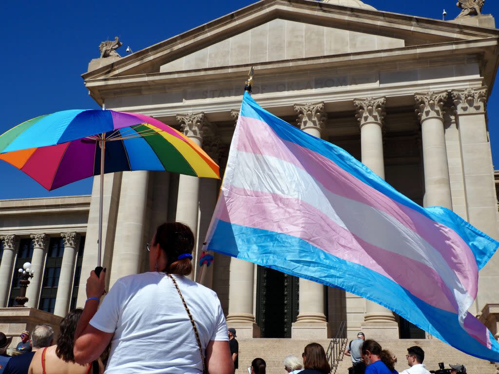 A person holds the transgender flag and a rainbow umbrella outside the Oklahoma State Capitol in Oklahoma City on March 14, 2024. More than 100 people gathered for a march honoring nonbinary teenager Nex Benedict, who died Feb. 8 by suicide.