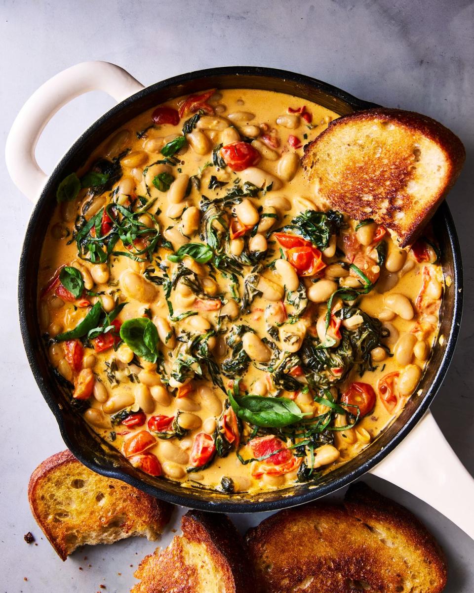 cast iron skillet filled with creamy tuscan white beans topped with basil, with toast alongside