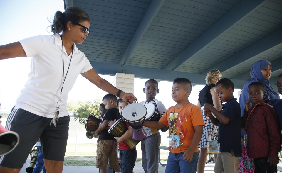 Teacher Linda Patterson, left, hands a drum to Roberto Gomez Ruiz, middle, as his classmates look on at Valencia Newcomer School Thursday, Oct. 17, 2019, in Phoenix. Children from around the world are learning the English skills and American classroom customs they need to succeed at so-called newcomer schools. Valencia Newcomer School in Phoenix is among a handful of such public schools in the United States dedicated exclusively to helping some of the thousands of children who arrive in the country annually. (AP Photo/Ross D. Franklin)