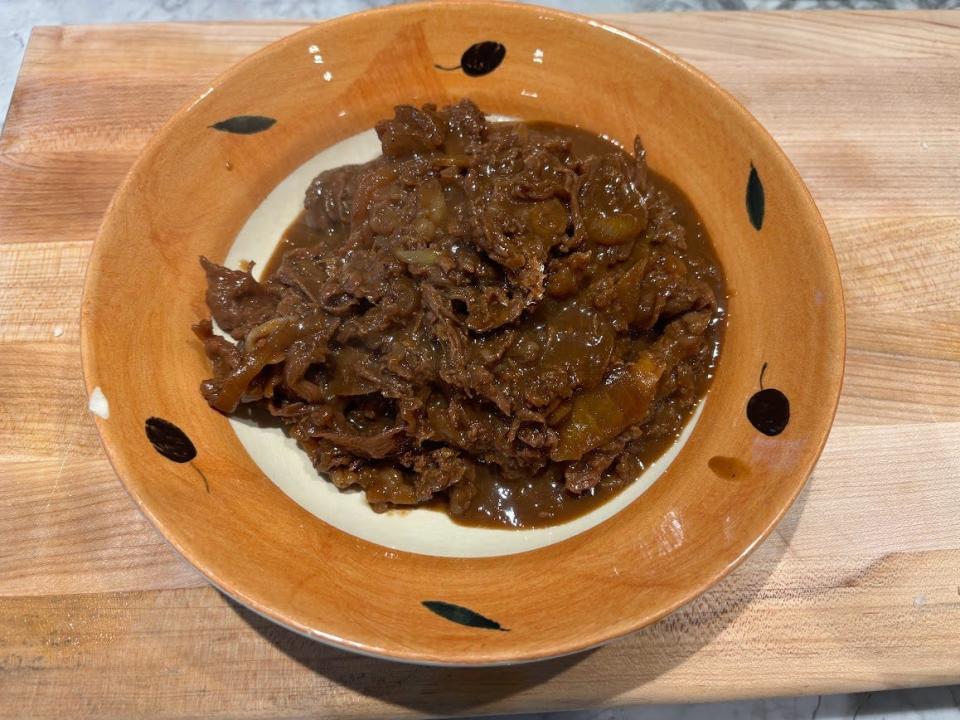 Cooked beef bulgogi on a white and orange plate with black design on the edge of the plate on a wooden cutting board