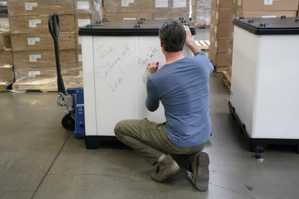 FILE - Gov. Gavin Newsom writes "From California with Love," on the side of shipping container he helped load with medical supplies bound for the Ukraine, at the Office of Emergency Services warehouse in Sacramento, Calif., on March 15, 2022. Driven by moral outrage over Russia’s invasion of Ukraine, U.S. governors and other top state officials made it clear: They wanted to cut any financial ties with Russia. (AP Photo/Rich Pedroncelli, File)