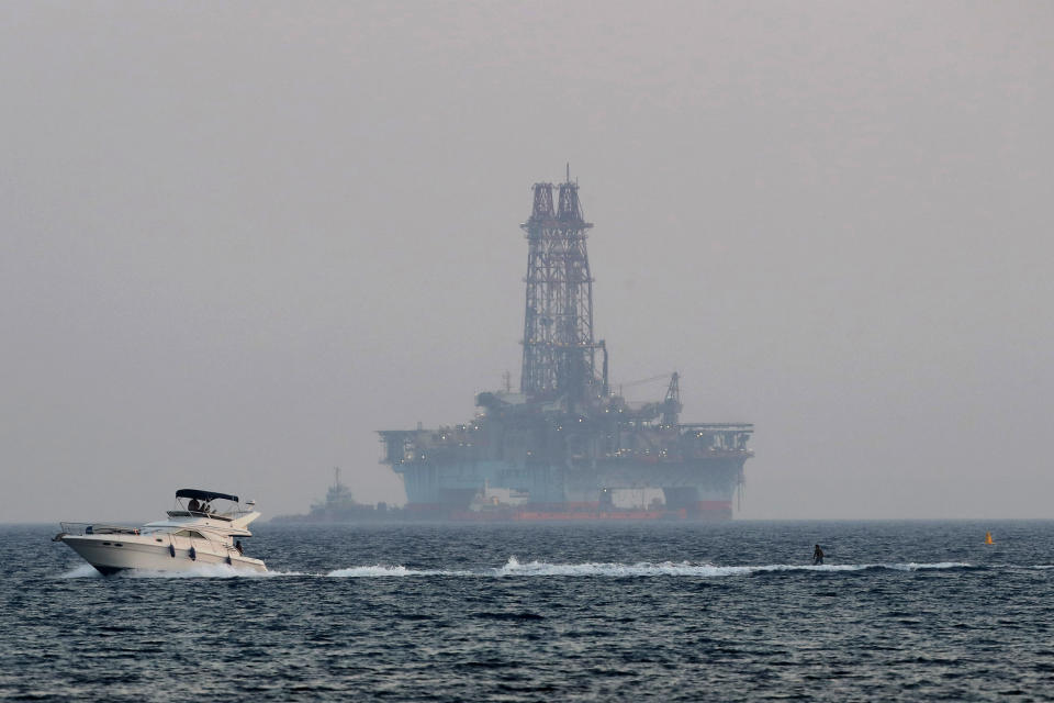 An offshore drilling rig is seen in the waters off Cyprus' coastal city of Limassol, Sunday, July 5, 2020 as a boat passes with a skier. Russian President Vladimir Putin has promised to intercede with Turkey to try and ease rising tensions over its oil and gas exploration in eastern Mediterranean waters that Cyprus claims as its own, the Cypriot government said Thursday, July 30, 2020. (AP Photo/Petros Karadjias)