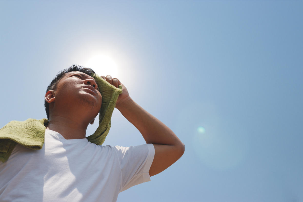 Seen from below, a person wipes their brow with a towel beneath the sun.