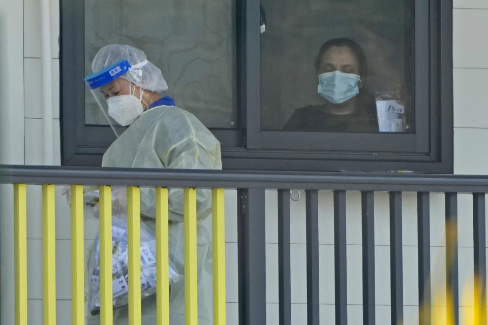 FILE - A woman receives materials from a worker at an isolation unit at the Penny's Bay Quarantine Centre on Lantau Island, in Hong Kong on Feb. 24, 2022. The fast-spreading omicron variant is overwhelming Hong Kong, prompting mass testing, quarantines, supermarket panic-buying and a shortage of hospital beds. Even the morgues are overflowing, forcing authorities to store bodies in refrigerated shipping containers. (AP Photo/Kin Cheung, File)