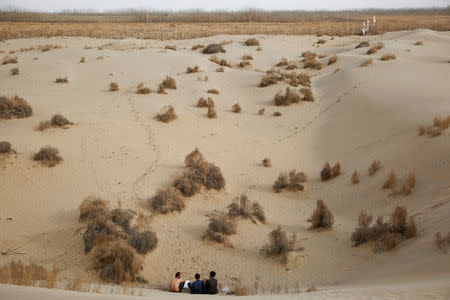 Men sit at the foot of a dune in the Taklamakan Desert outside the village of Jiya near Hotan, Xinjiang Uighur Autonomous Region, China, March 21, 2017. REUTERS/Thomas Peter