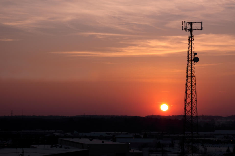 A single cell tower in stark silhouette against a colorful sunrise.