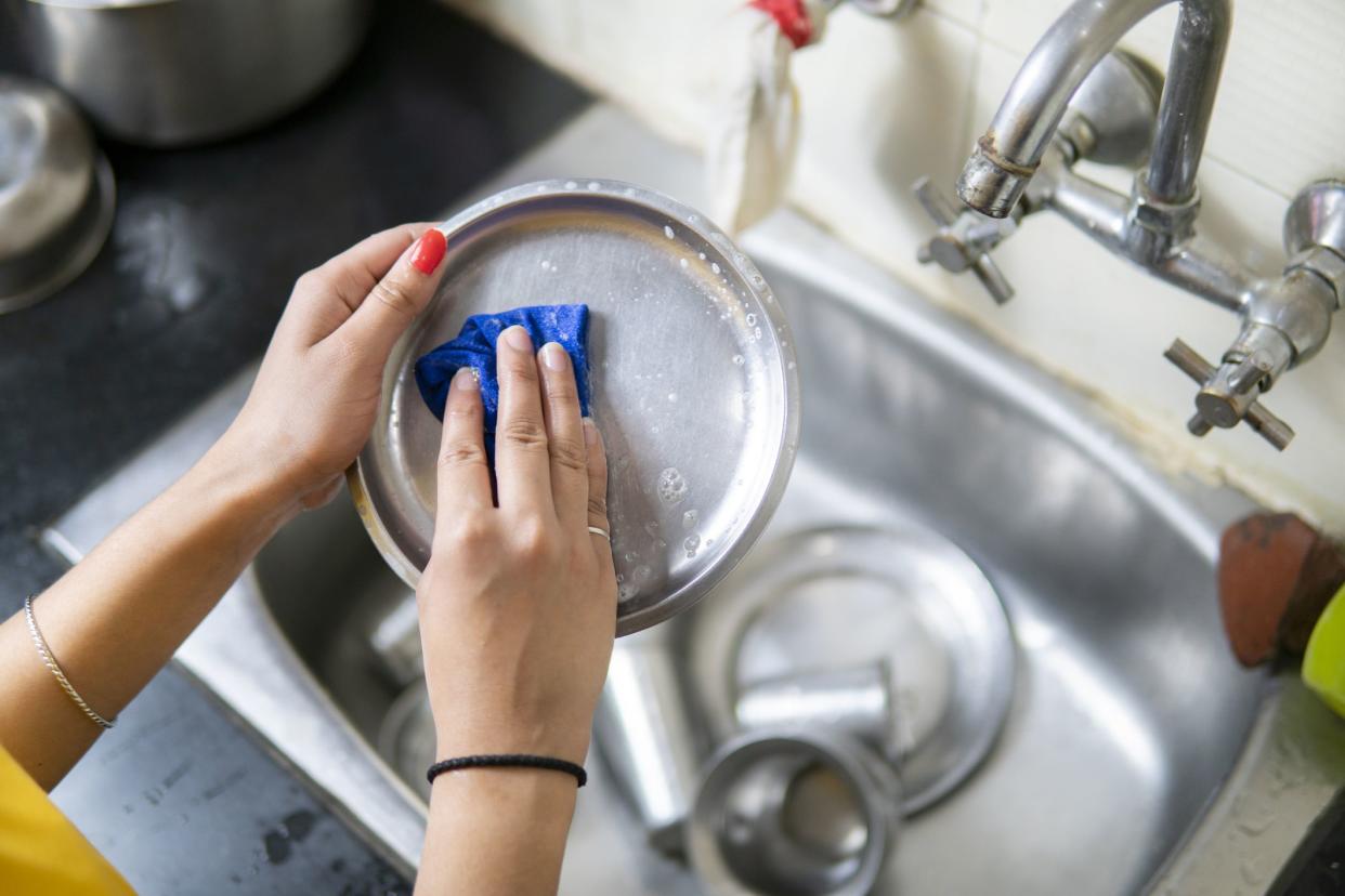 High angle close-up of woman's hand washing utensils over the sink at kitchen.