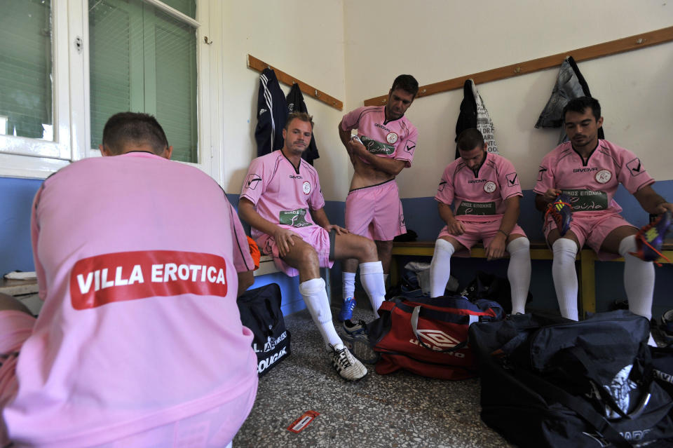 In this photo taken Sunday, Oct. 7, 2012, Voukefalas players, a small amateur soccer club, get ready in a changing room before a local championship match in the city of Larissa, central Greece. A cash-strapped Greek soccer team has found a new way to pay the bills, with help from the world’s oldest profession. Players are wearing bright pink practice jerseys emblazoned with the logos of the Villa Erotica and Soula’s House of History, a pair of pastel-colored bordellos recruited to sponsor the team after drastic government spending cuts left the country's sports organizations facing ruin. One team took on a deal with a local funeral home and others have wooed kebab shops, a jam factory, and producers of Greece’s trademark feta cheese. But the small amateur Voukefalas club which includes students, a bartender, waiters and pizza delivery drivers is getting the most attention for its flamboyant sponsors. (AP Photo/Nikolas Giakoumidis)