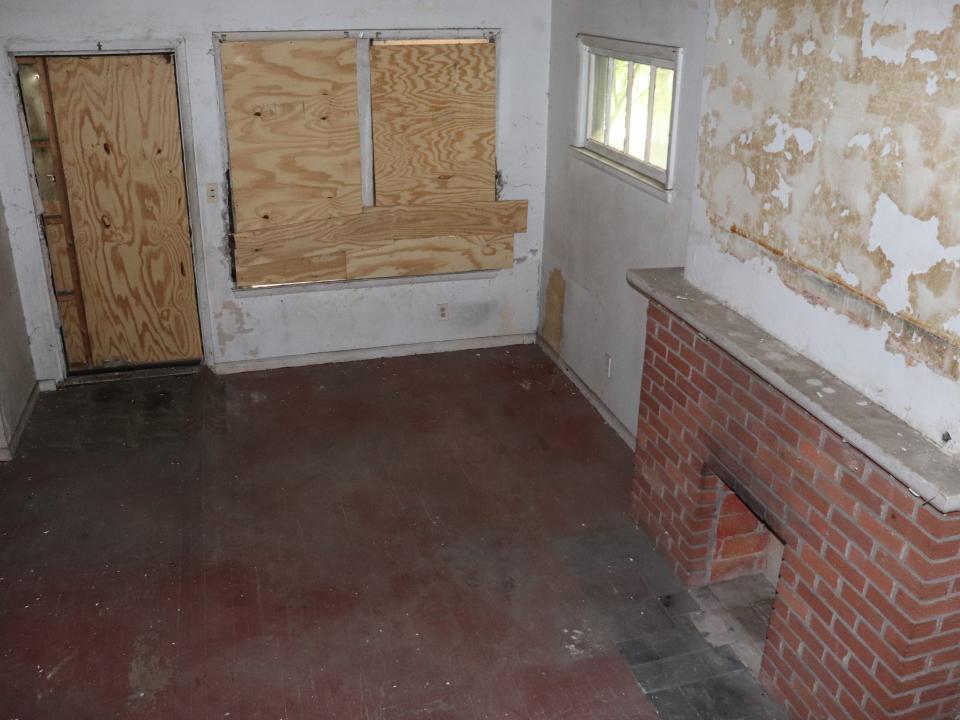 An abandoned living room where the windows and door are boarded up.