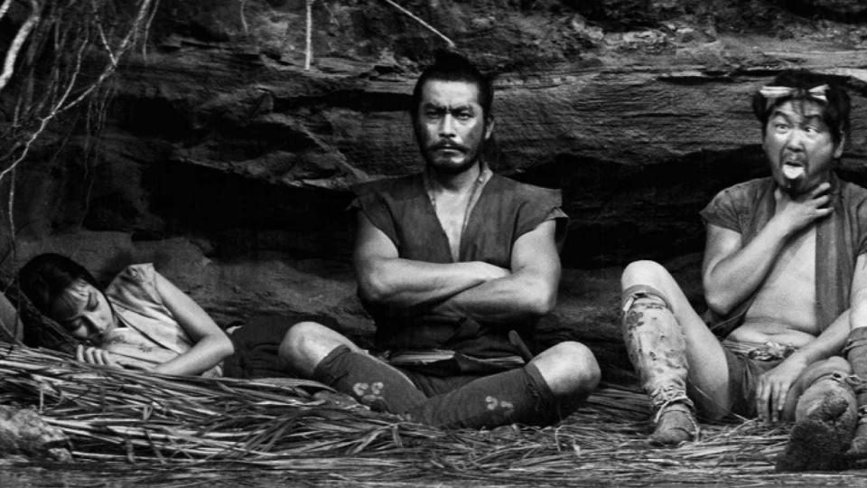 A still from The Hidden Fortress shows Toshiro Mifune sitting between a sleeping woman and man pulling a silly face