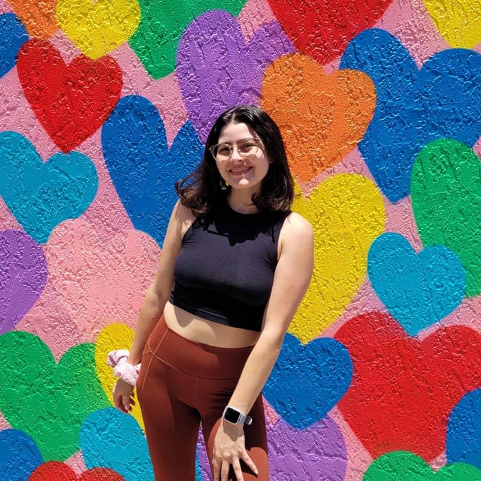 Nai'a μπροστά από έναν τοίχο ζωγραφισμένο με καρδιές στο ουράνιο τόξο