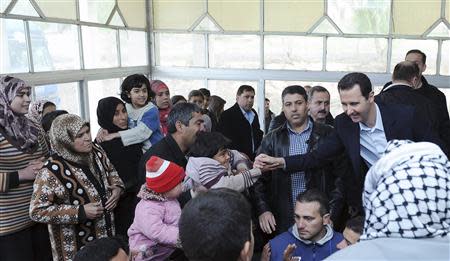 Syria's President Bashar al-Assad holds the hand of a child during his visit to displaced Syrians in the town of Adra in the Damascus countryside March 12, 2014, in this handout photograph released by Syria's national news agency SANA. REUTERS/SANA/Handout via Reuters