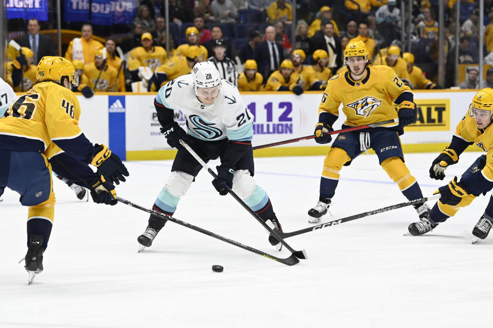 Seattle Kraken right wing Eeli Tolvanen (20) maneuvers the puck between Nashville Predators defenseman Jordan Gross (46) and center Cody Glass (8) during the first period of an NHL hockey game Thursday, March 23, 2023, in Nashville, Tenn. (AP Photo/Mark Zaleski)