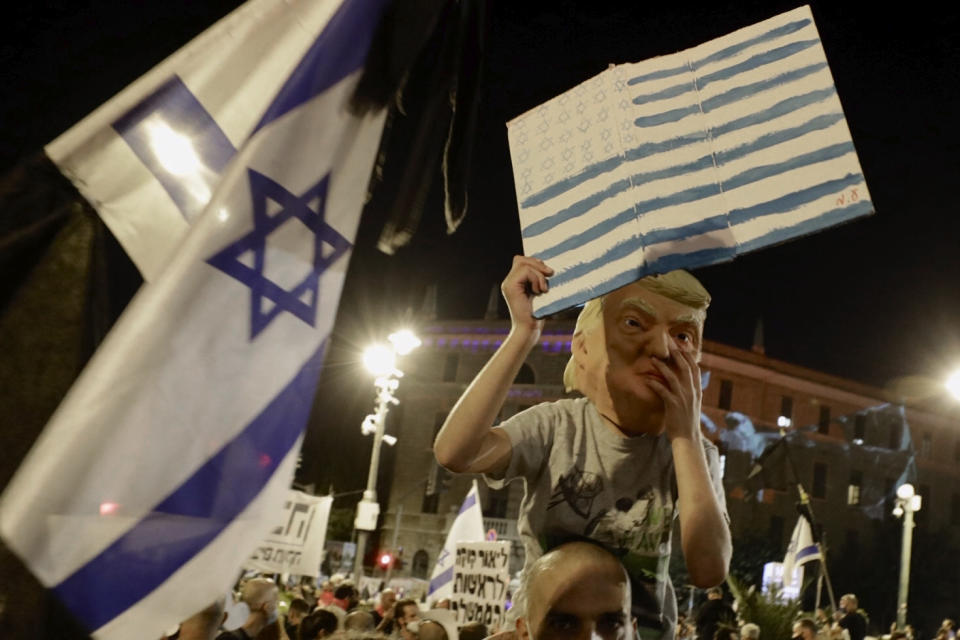 An Israeli wears a US President Mask as Israeli protesters chant slogans during a demonstration against Israeli Prime Minister Benjamin Netanyahu outside the Prime Minister's residence in Jerusalem, Saturday, Sept. 12, 2020. (AP Photo/Sebastian Scheiner)