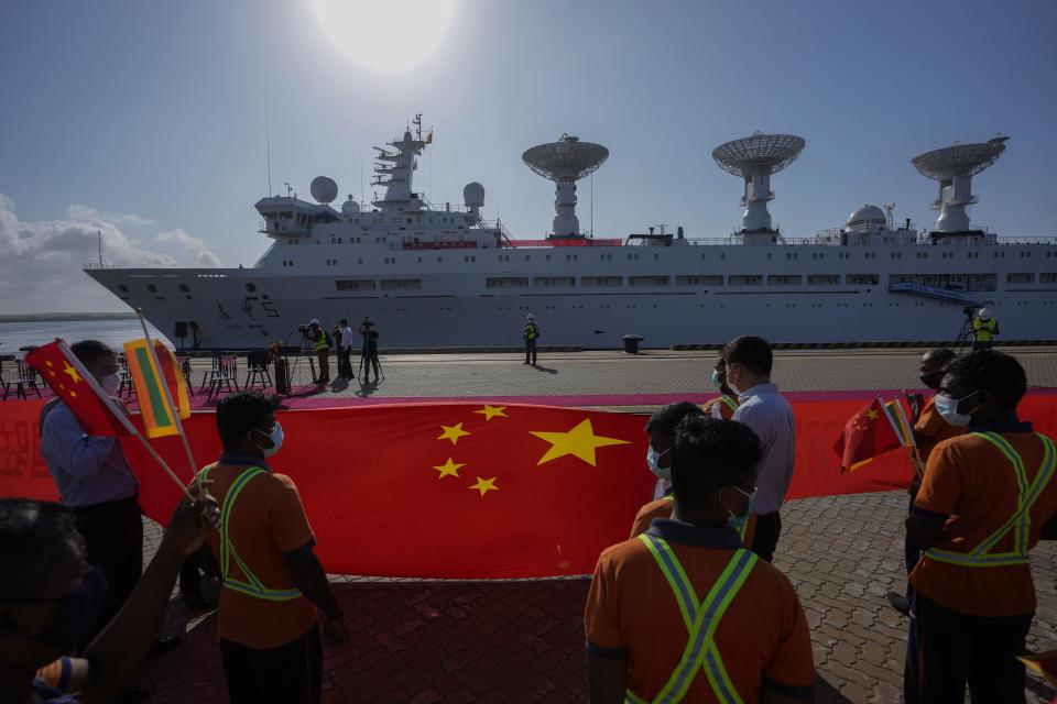 Sri Lankan port workers hold a Chinese national flag to welcome Chinese research ship Yuan Wang 5 as it arrives in Hambantota International Port in Hambantota, Sri Lanka, Tuesday, Aug. 16, 2022. The ship was originally set to arrive Aug. 11 but the port call was deferred due to apparent security concerns raised by India. (AP Photo/Eranga Jayawardena)