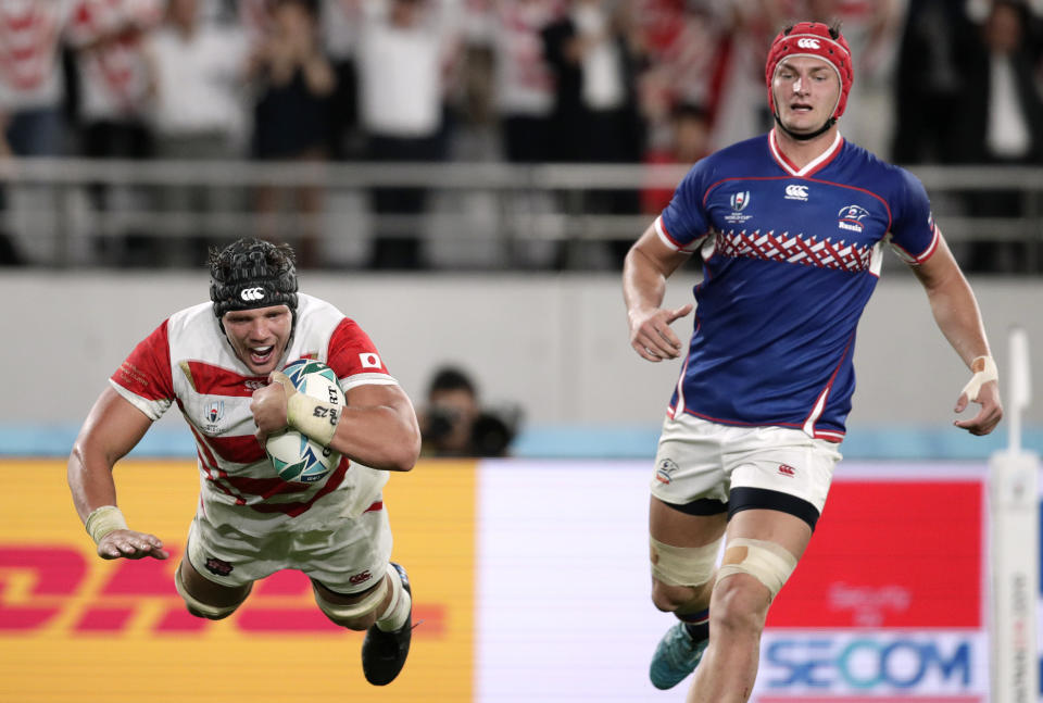 Japan's Pieter Labuschagne, left, is airborne as he scores a try as Russia's Bogdan Fedotko, right, watches during the Rugby World Cup Pool A game at Tokyo Stadium between Russia and Japan in Tokyo, Japan, Friday, Sept. 20, 2019. (AP Photo/Jae Hong)