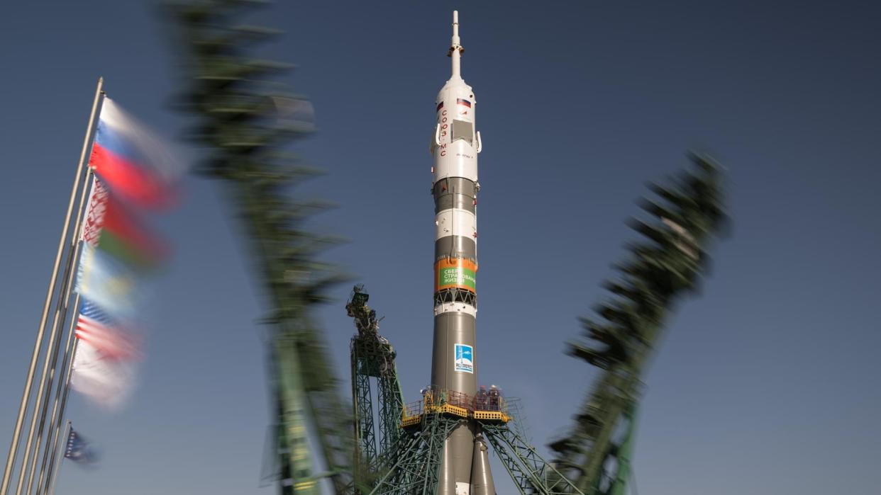  A brown-and-white rocket stands upright on a launch pad as two metallic skeletal structures fall away from it. 