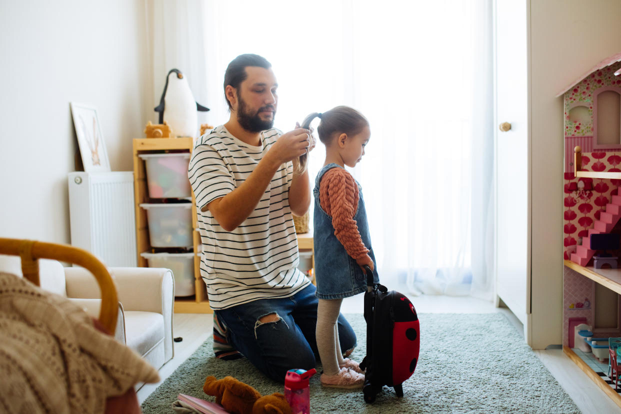 Father combing, brushing his daughter's hair at home, father and daughter smiling, family moments, spending time together.