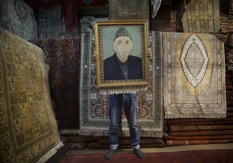 FILE - In this Sunday, March 30, 2014 file photo made by Associated Press photographer Anja Niedringhaus, an Afghan carpet seller holds up a framed carpet depicting Afghan President Hamid Karzai in his store in Kabul, Afghanistan. Niedringhaus, 48, an internationally acclaimed German photographer, was killed and an AP reporter was wounded on Friday, April 4, 2014 when an Afghan policeman opened fire while they were sitting in their car in eastern Afghanistan. (AP Photo/Anja Niedringhaus, File)