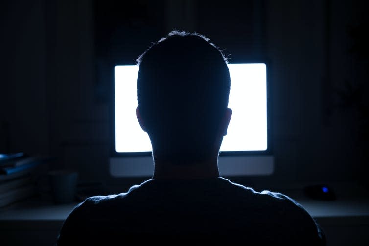 The back of a person&#39;s head looking at a computer screen in the dark.