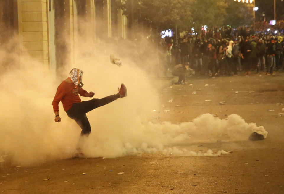 An anti-government protester kicks back a tear gas canister against the riot police, during a protest near the parliament square, in downtown Beirut, Lebanon, Sunday, Dec. 15, 2019. Lebanese security forces fired tear gas, rubber bullets and water cannons Sunday to disperse hundreds of protesters for a second straight day, ending what started as a peaceful rally in defiance of the toughest crackdown on anti-government demonstrations in two months. (AP Photo/Hussein Malla)