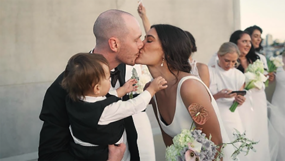 Lachlan holding his son while kissing his wife on their wedding day in June.