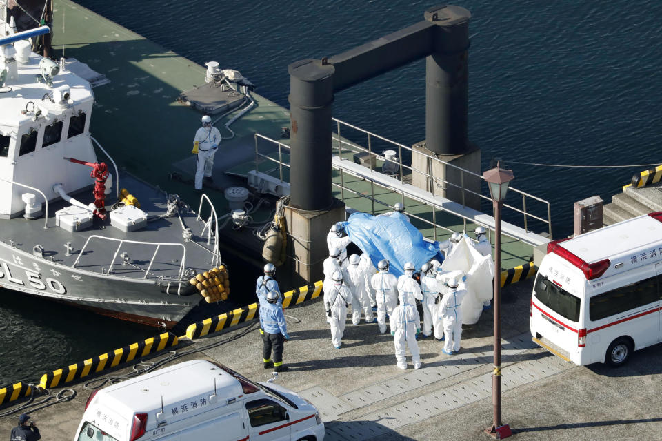 Medical workers in protective suits lead a passenger tested positive for a new coronavirus from the cruise ship Diamond Princess at Yokohama Port in Yokohama, south of Tokyo, Wednesday, Feb. 5, 2020. Japan said Wednesday 10 people on the cruise ship have tested positive for the new virus and were being taken to hospitals. Health Minister Nobukatsu Kato said all the 3,700 people and passengers on the ship will be quarantined on board for up to 14 days under Japanese law. (Hiroko Harima/Kyodo News via AP)