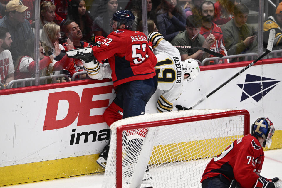 Washington Capitals defenseman Dylan McIlrath (52) and Boston Bruins center John Beecher (19) collide along the boards during the third period of an NHL hockey game, Monday, April 15, 2024, in Washington. Capitals goaltender Charlie Lindgren looks on. (AP Photo/Nick Wass)