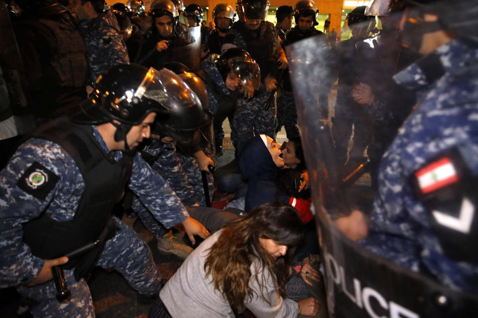 Protesters lie on a road, as they scream and hold each others while riot police try to remove them and open the road, in Beirut, Lebanon, Wednesday, Dec. 4, 2019. Protesters have been holding demonstrations since Oct. 17 demanding an end to corruption and mismanagement by the political elite that has ruled the country for three decades. (AP Photo/Bilal Hussein)