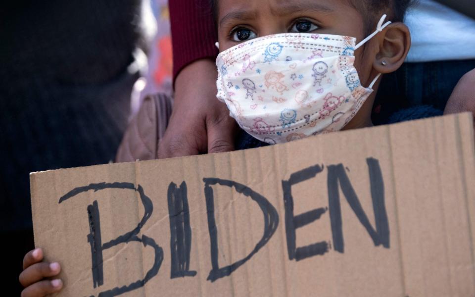 Dareli Matamoros, a girl from Honduras, holds a sign asking President Joe Biden to let her in at a border crossing in Tijuana - GUILLERMO ARIAS /AFP