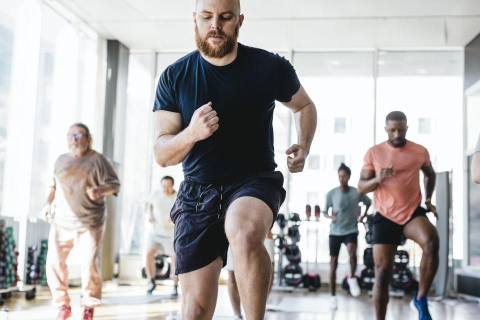 determined man practicing jogging with male friends during exercise class in gym