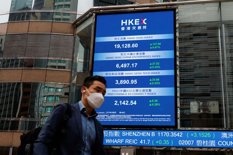 A man walks past a screen displaying the Hang Seng Index at Central district, in Hong Kong