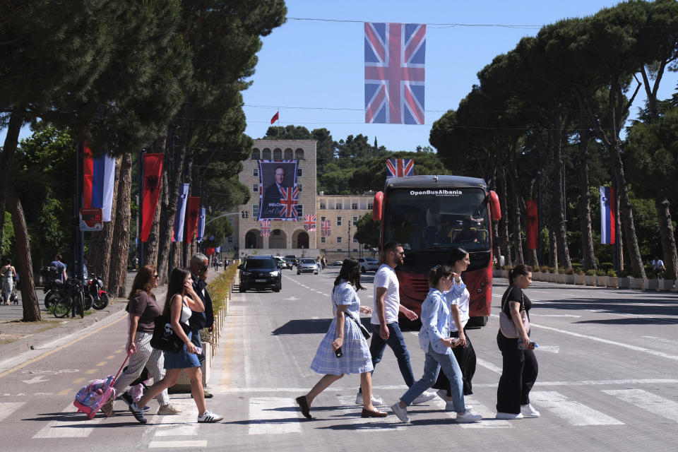 Pedestrians cross an avenue as a portrait of British Foreign Secretary David Cameron is attached on a facade at the Tirana University, in Tirana, Albania, Wednesday, May 22, 2024. British Foreign Secretary David Cameron has hailed progress in a U.K.-Albania joint effort to cut illegal migration, saying small boat arrivals from Albania to the U.K. fell by over 90% in 2023, as the two countries fought people smuggling gangs. (AP Photo/Vlasov Sulaj)