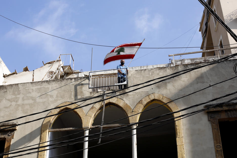 FILE - In this Friday, Aug. 7, 2020, file photo, a man puts a Lebanese flag on the roof of a damaged building at a neighborhood near the scene of an explosion several days earlier that hit the seaport of Beirut, Lebanon. After a massive explosion ripped through Beirut this month, clinical psychologist Yorgo Younes knew he had to step forward and help his fellow citizens deal with the psychological toll. Online, Younes and others offered to help those grappling with the trauma of a blast that devastated a people already wearied by the coronavirus pandemic and severe economic turmoil. (AP Photo/Thibault Camus, File)