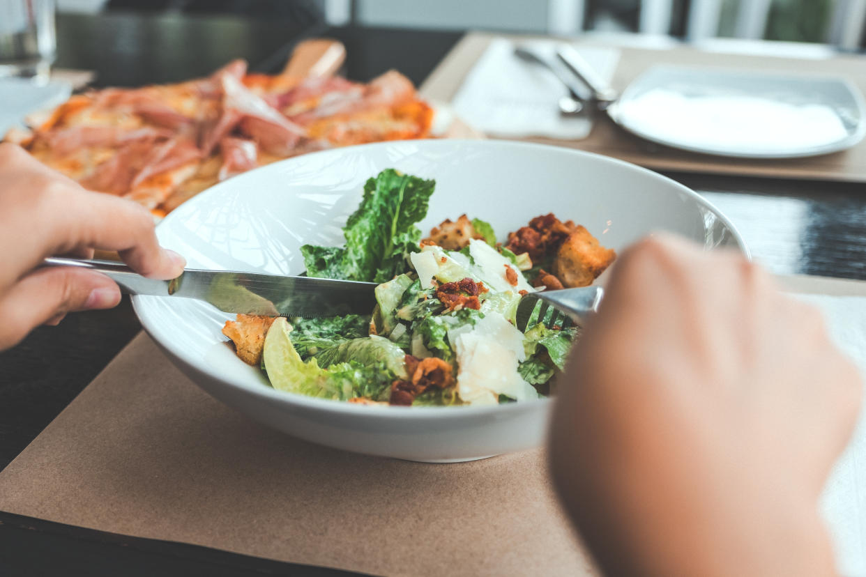 A hand using fork and knife to eat Ceasar salad with pizza on dining table in the restaurant girl dinner