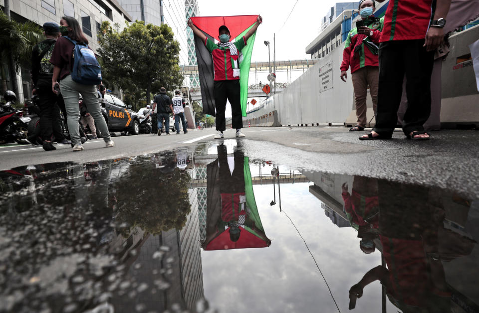 An image of a protester holding up a Palestinian flag is reflected in water on a street as he poses for photographers during a rally condemning Israeli attacks on the Palestinians, in Jakarta, Indonesia, Tuesday, May 18, 2021. (AP Photo/Dita Alangkara)