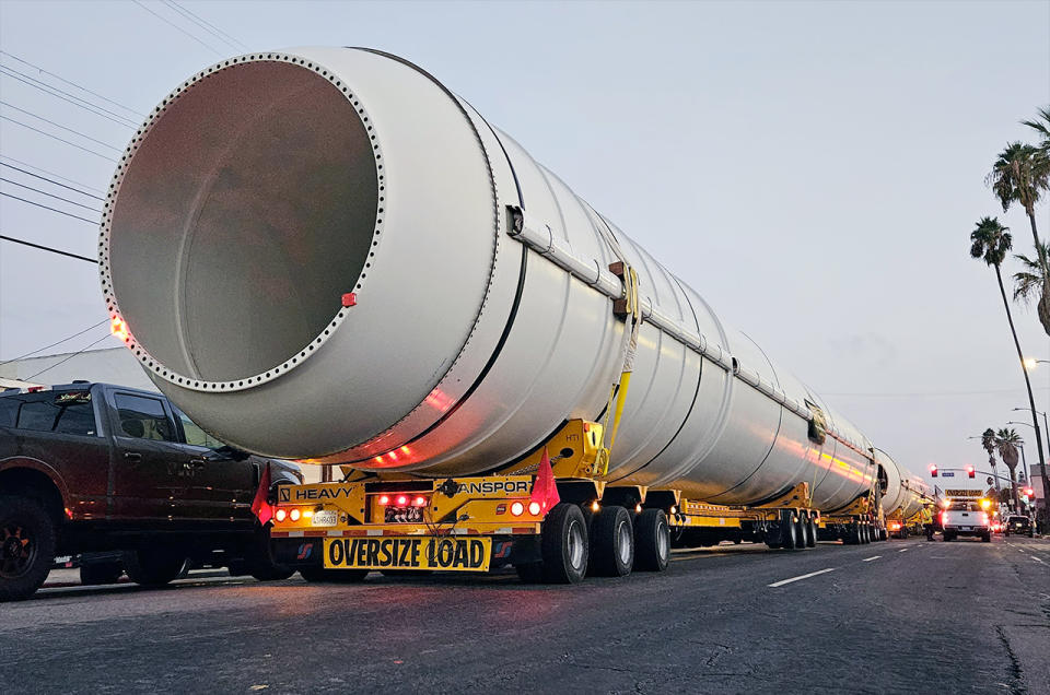 close-up of the end of a white, cylindrical solid rocket motor being towed by truck on a city street.