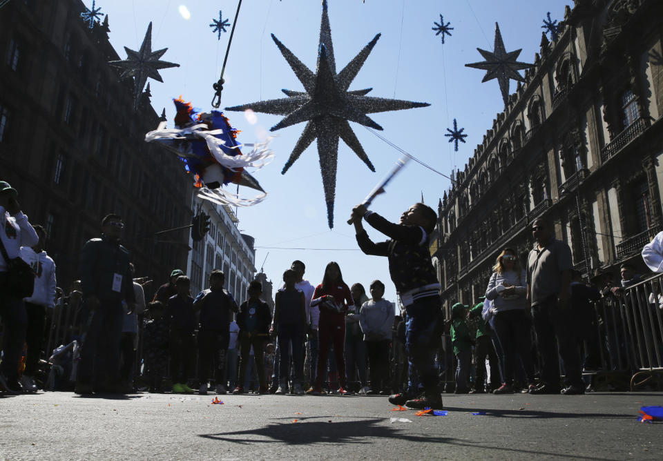 FILE - A girl swings at a traditional Christmas piñata filled with fruit and candy during the Epiphany, or Three Kings Day, celebrations at the Zocalo plaza in Mexico City, Monday, Jan. 6, 2020. Epiphany, the 12th night of Christmas, marks the day the three wise men visited baby Jesus. (AP Photo/Marco Ugarte, File)