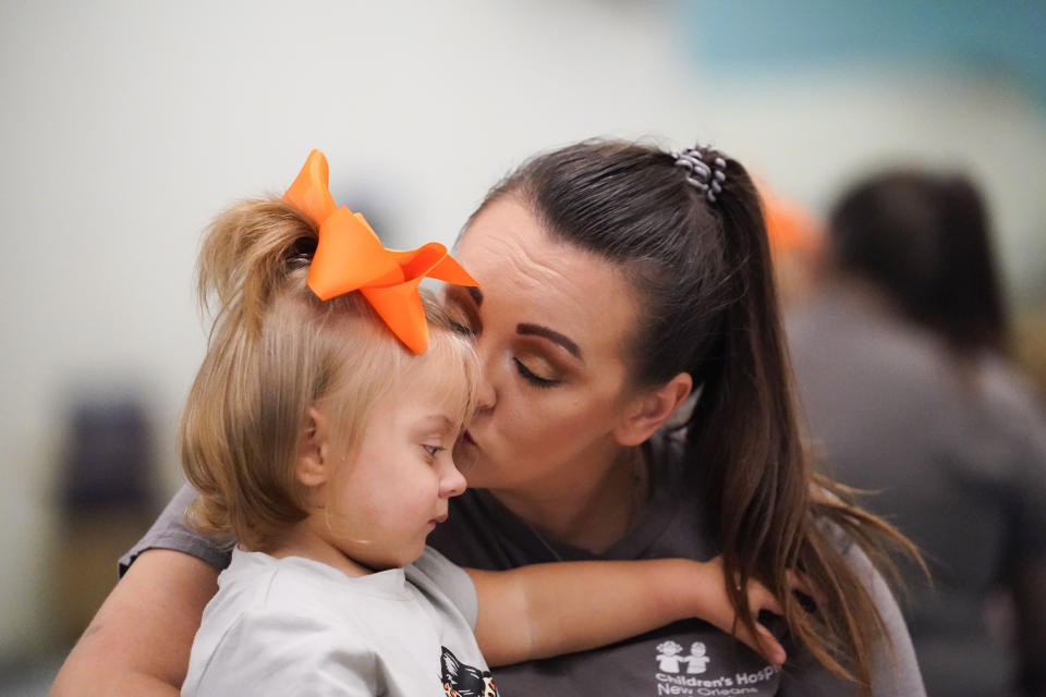 Heather Hampton kisses her daughter Freya Baudoin,18 months, as she is introduced to her mobility chair for the first time, at the Children's Hospital New Orleans Rehabilitation Center, in Metairie, La., Monday, Oct. 30, 2023. Tulane science and engineering students are making the second batch of mobility chairs for toddlers, that will eventually go to pediatric patients at Children's Hospital. Wheelchairs are expensive, and insurance won't cover the cost for children unless the child proves they can operate it independently. (AP Photo/Gerald Herbert)