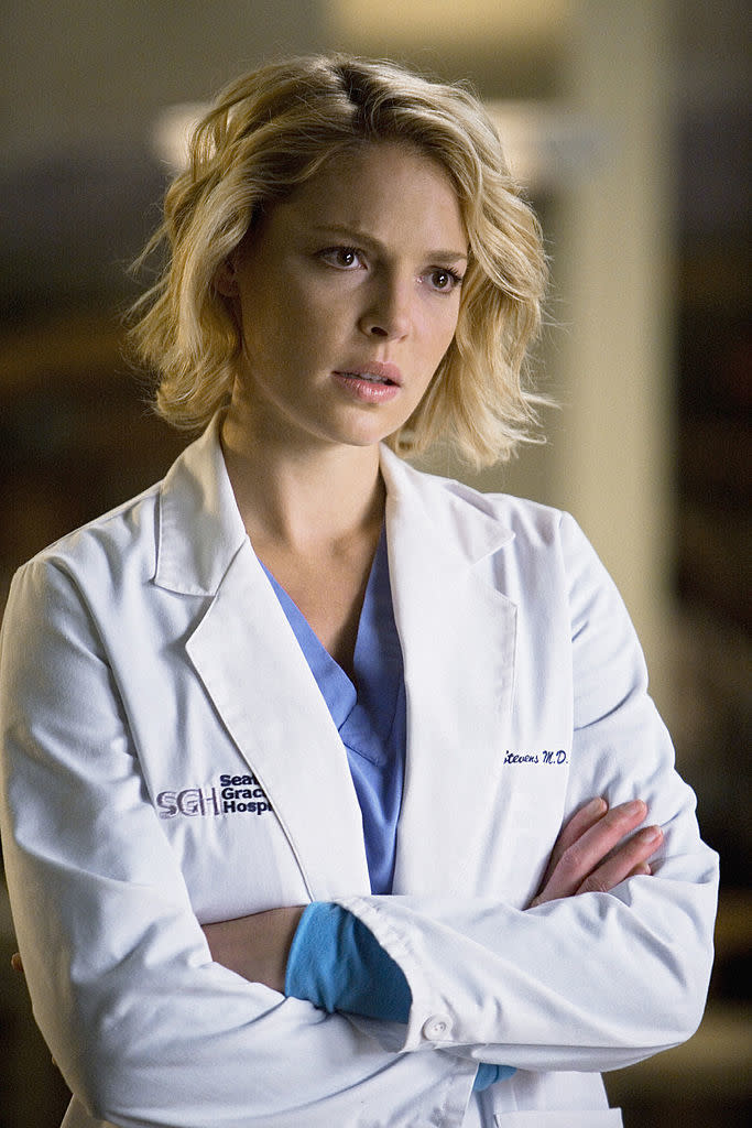 Katherine Heigl as Dr. Izzie Stevens in "Grey's Anatomy," wearing a white doctor's coat with folded arms, looking concerned