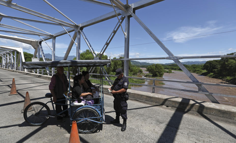 Un policía revisa los papeles de tres personas en un puente que une El Salvador con Guatemala en la localidad salvadoreña de La Hachadura el 11 de octubre del 2019. El control de la frontera se ha endurecido desde que varios países centroamericanos firmaron acuerdos con EEUU para reducir la emigración. (AP Photo/Eduardo Verdugo)