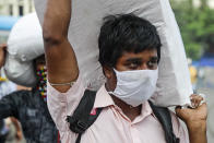 A man wearing a face mask carries a load on his shoulder as he walks to catch a bus in Kolkata, India, Friday, Aug. 14, 2020. India's coronavirus death toll overtook Britain's to become the fourth-highest in the world with another single-day record increase in cases Friday. (AP Photo/Bikas Das)