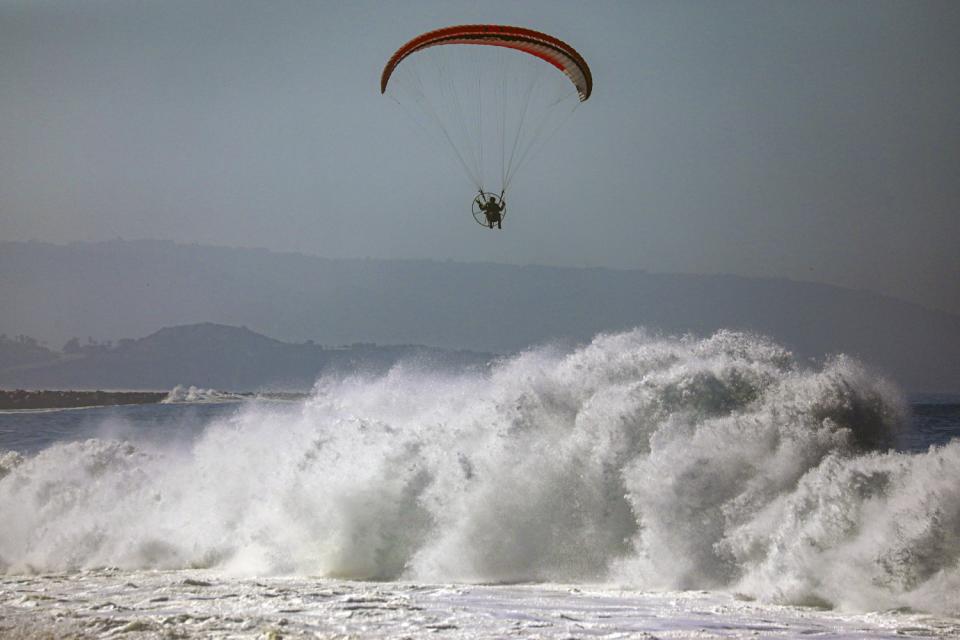 A powered paraglider flies above high surf near the Balboa Pier in Newport Beach on July 4.